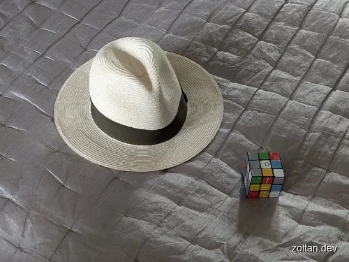 White straw hat and Rubik's cube on a quilted surface.