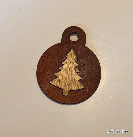 Circular keyring fob with a wooden cut-out Christmas tree design and hole at top for hanging.