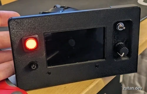 Close-up view of a black 3D-printed device with a red LED light, power button, and adjustable knob on its side panel.