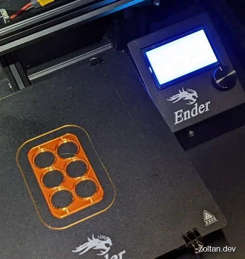 An Ender 3D printer displaying a partially printed coin holder on its bed.
