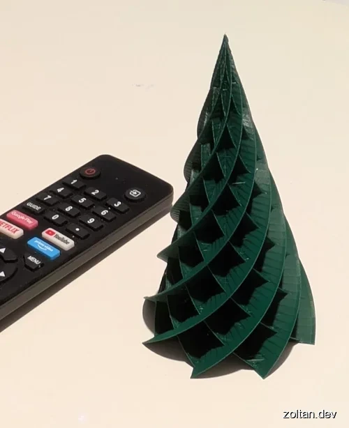 A green 3D-printed Christmas tree model next to a black TV remote control.