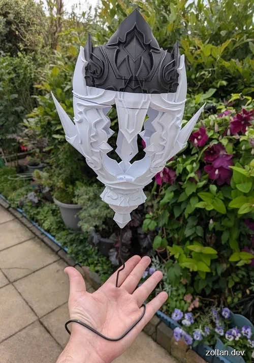 Hand holding a detailed 3D printed ornament with intricate designs and sharp edges against a backdrop of greenery and flowers.