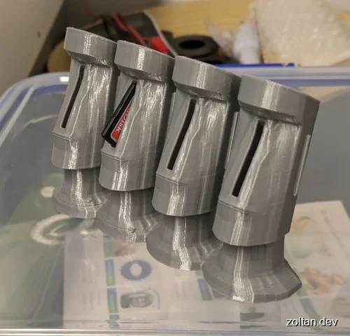 Four grey 3D-printed objects resembling Moai statue heads.