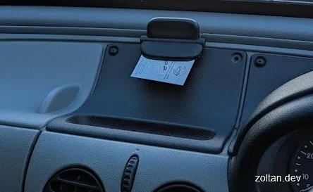 Close-up view of a car dashboard with a small paper clipped to a holder and various control buttons visible below it.