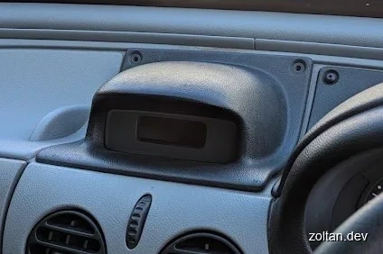Close-up view of a car's dashboard panel featuring a large hump with a small digital clock.