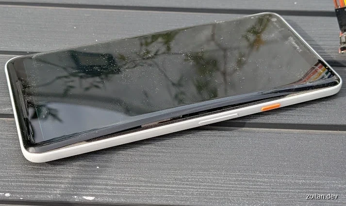 Damaged smartphone lying on a wooden surface with visible cracks and scratches on its screen.