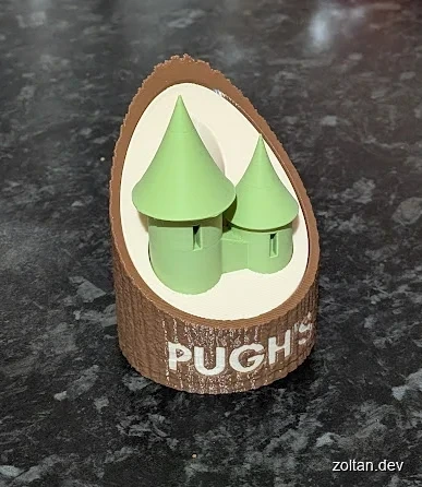 Two green cone-shaped objects resembling towers are displayed in a circular wooden holder labeled "PUGH'S" on a dark textured surface.