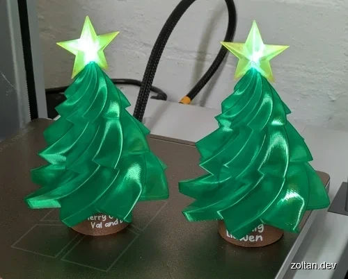 Two transparent green 3D-printed Christmas trees, with glowing star toppers rest on brown 3D printed bases, showcasing intricate design and vibrant finish.