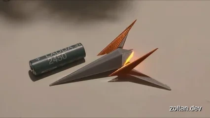A small Arwing model with orange fins and a glowing exhaust, alongside a cylindrical battery.
