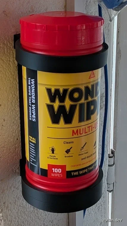 Red and yellow cylindrical container labeled "Wonder Wipes Multi-Use" with a black base, attached to a wall.