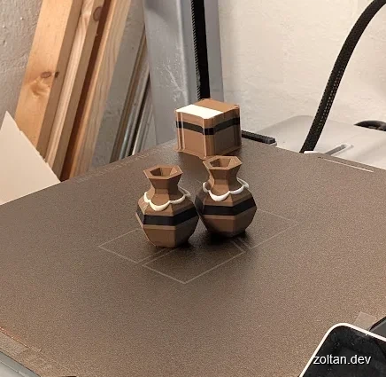 Three geometric 3D printed objects in brown and white sit on a Bambu Lab A1 3D printer.