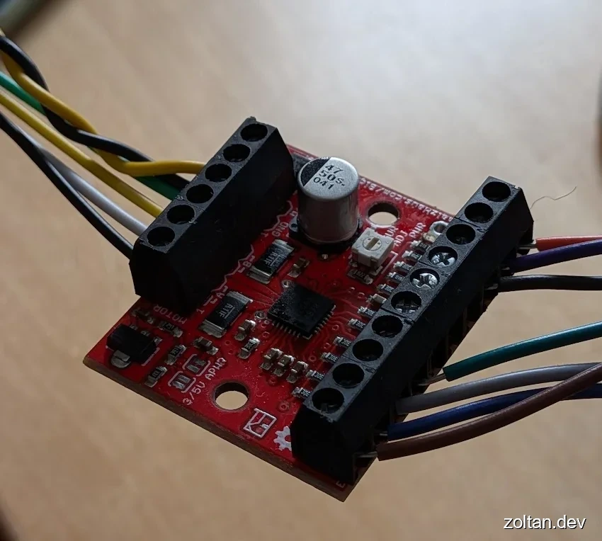 Close-up view of a red stepper motor control board with various electronic components and color-coded wires connected to it.