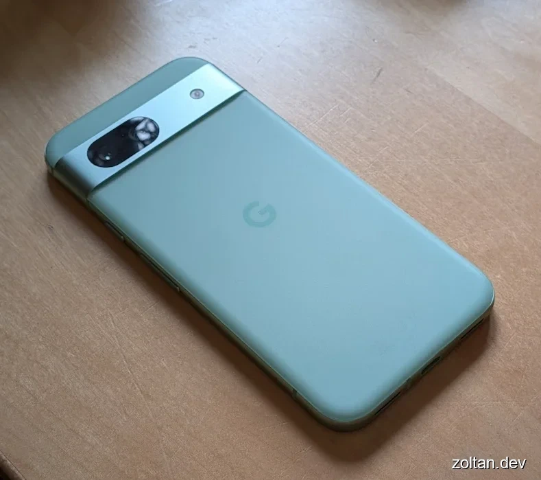 Back view of a Google Pixel 8a smartphone in Aloe green color, featuring a circular camera module and the Google logo on the back.